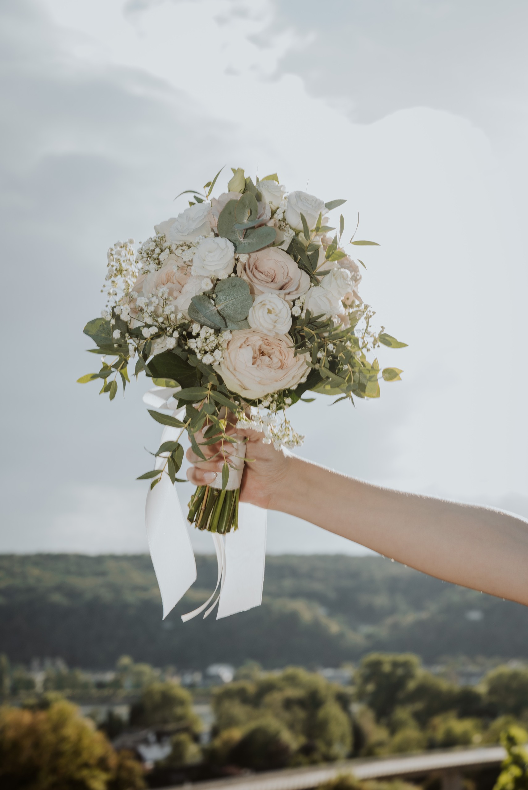 Leas Brautstrauß aus Rosen und Eukalyptus vor weitem Himmel.